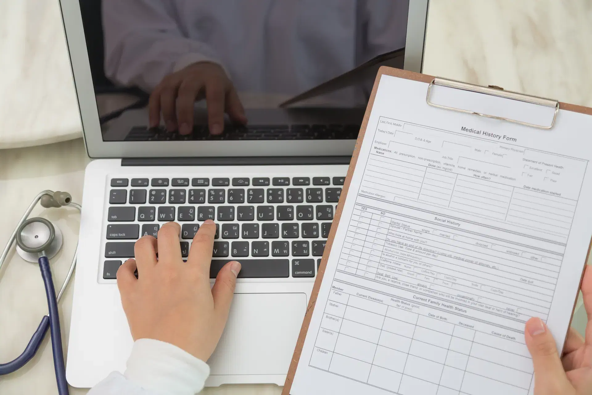 Doctor using laptop with clipboard